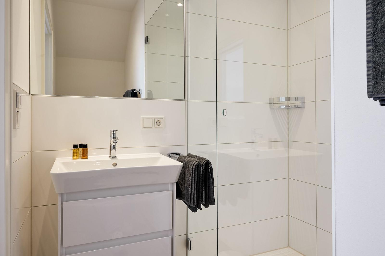 Badezimmer mit Dusche, Waschbecken und Spiegel