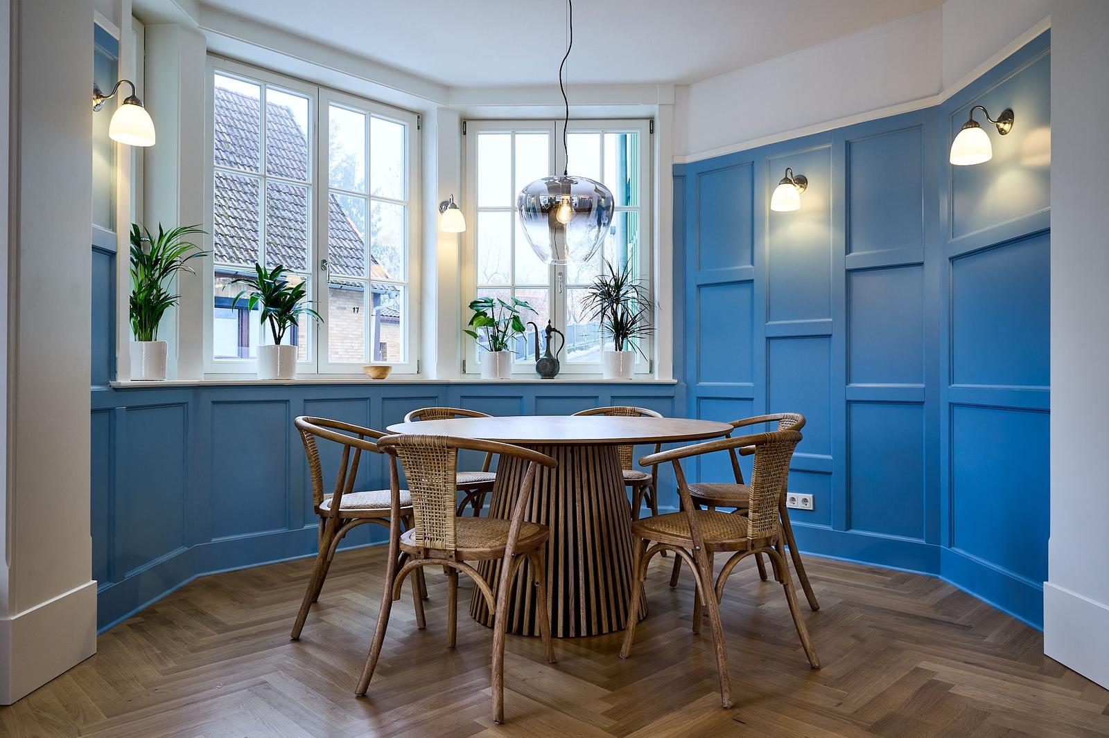 Esszimmer mit blauen Wänden, Holzboden und runden Tisch mit Stühlen.