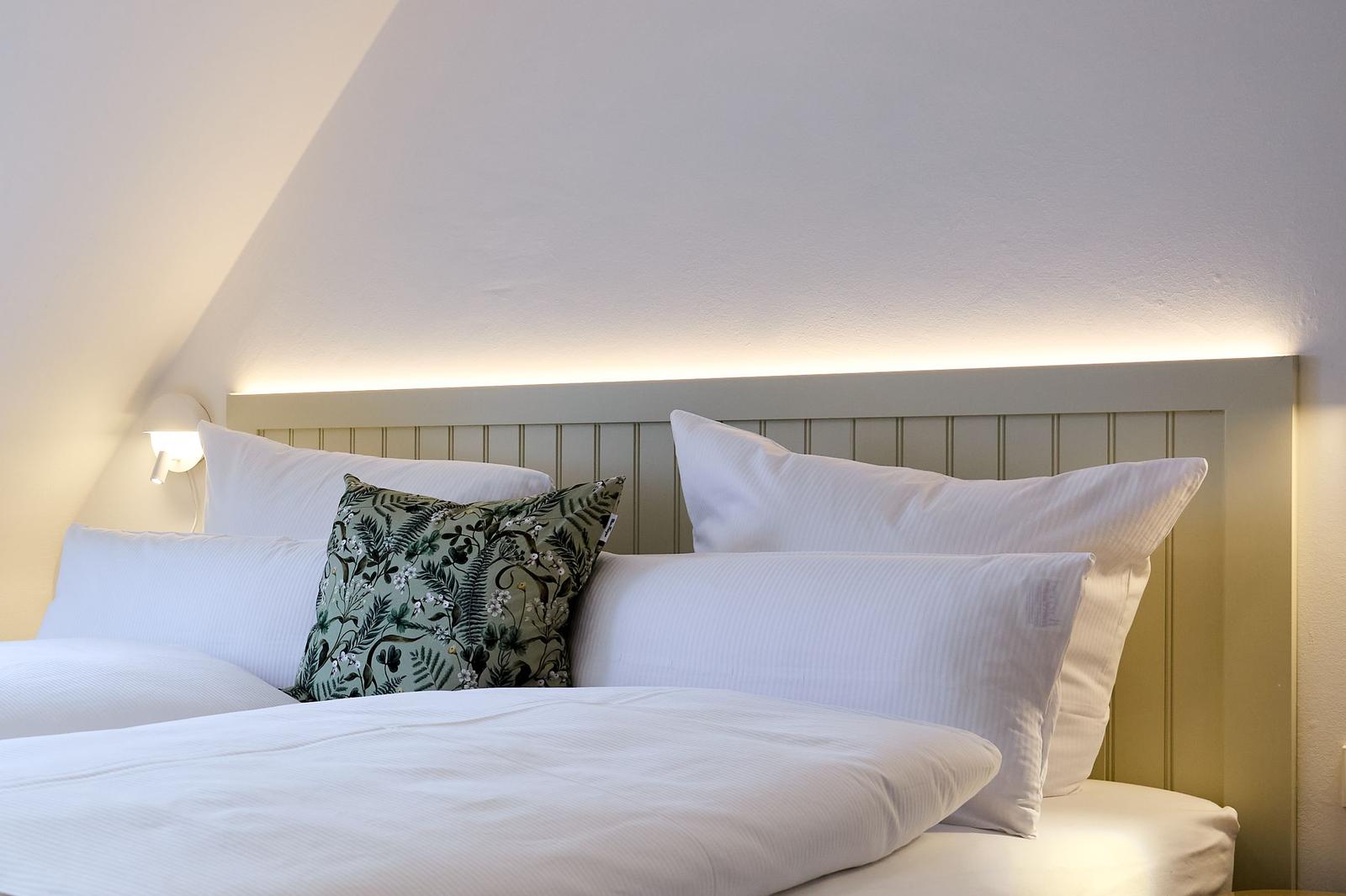 Doppelbett mit Kissen und gemusterter Kissenhülle unter schrägem Dach