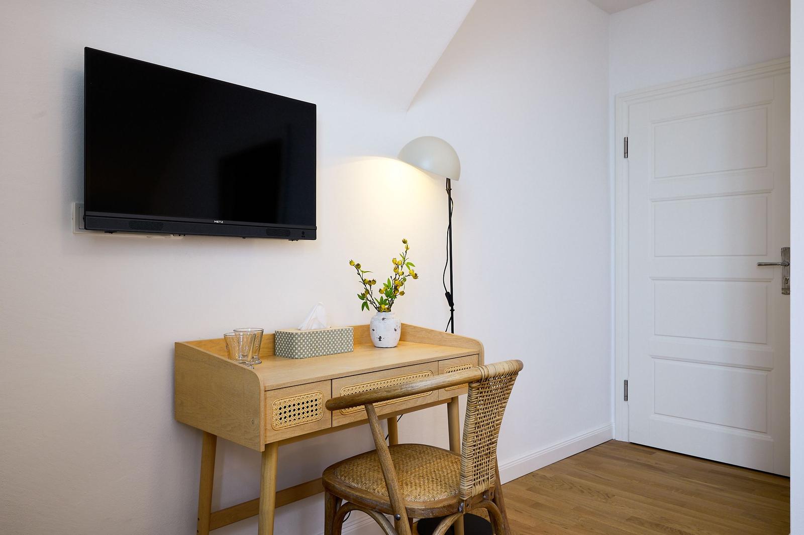 Schreibtisch mit Stuhl, Fernseher und Lampe in einem Raum mit Holzboden und weißer Tür.