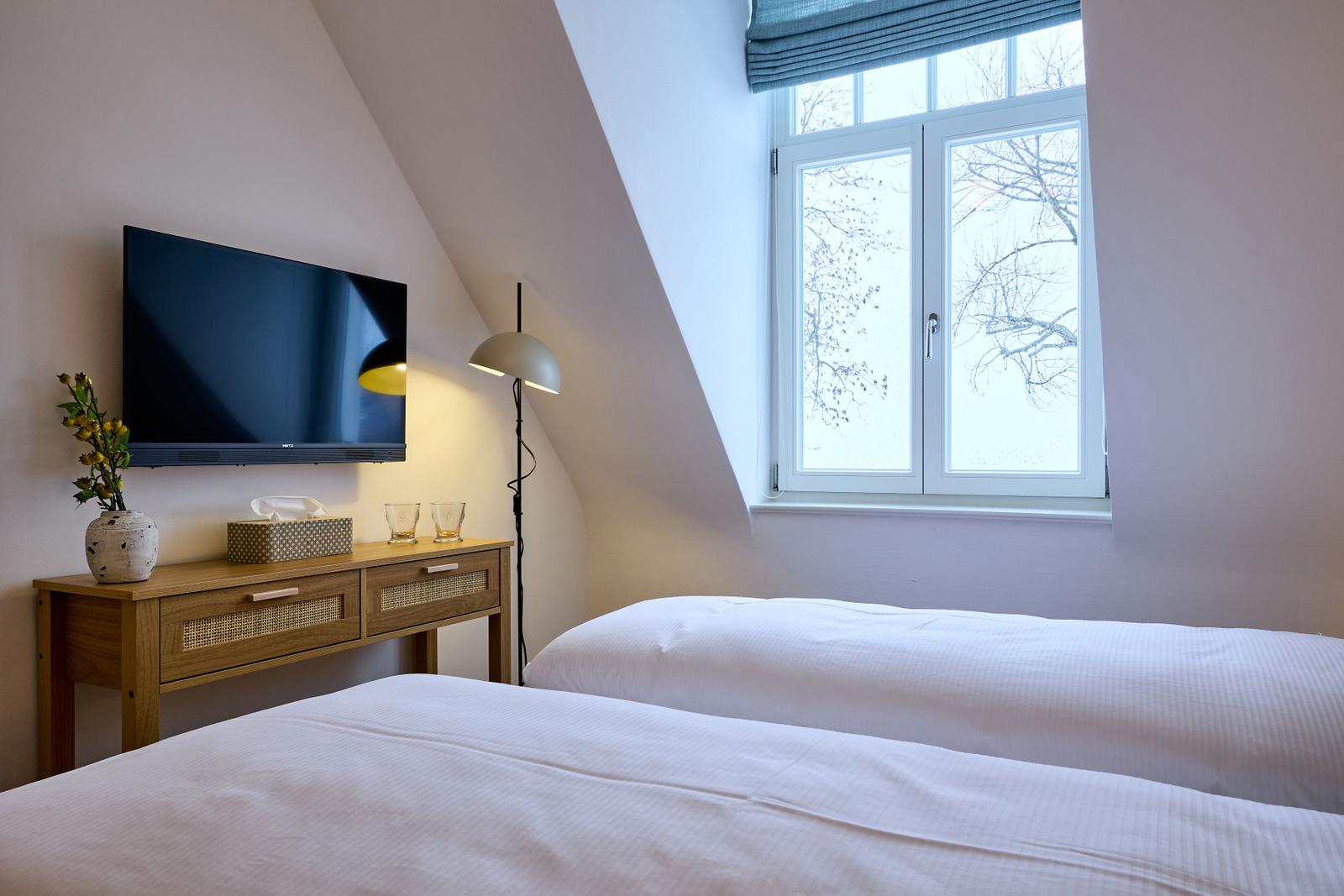 Zimmer mit Doppelbett, Fenster und Fernseher an der Wand.