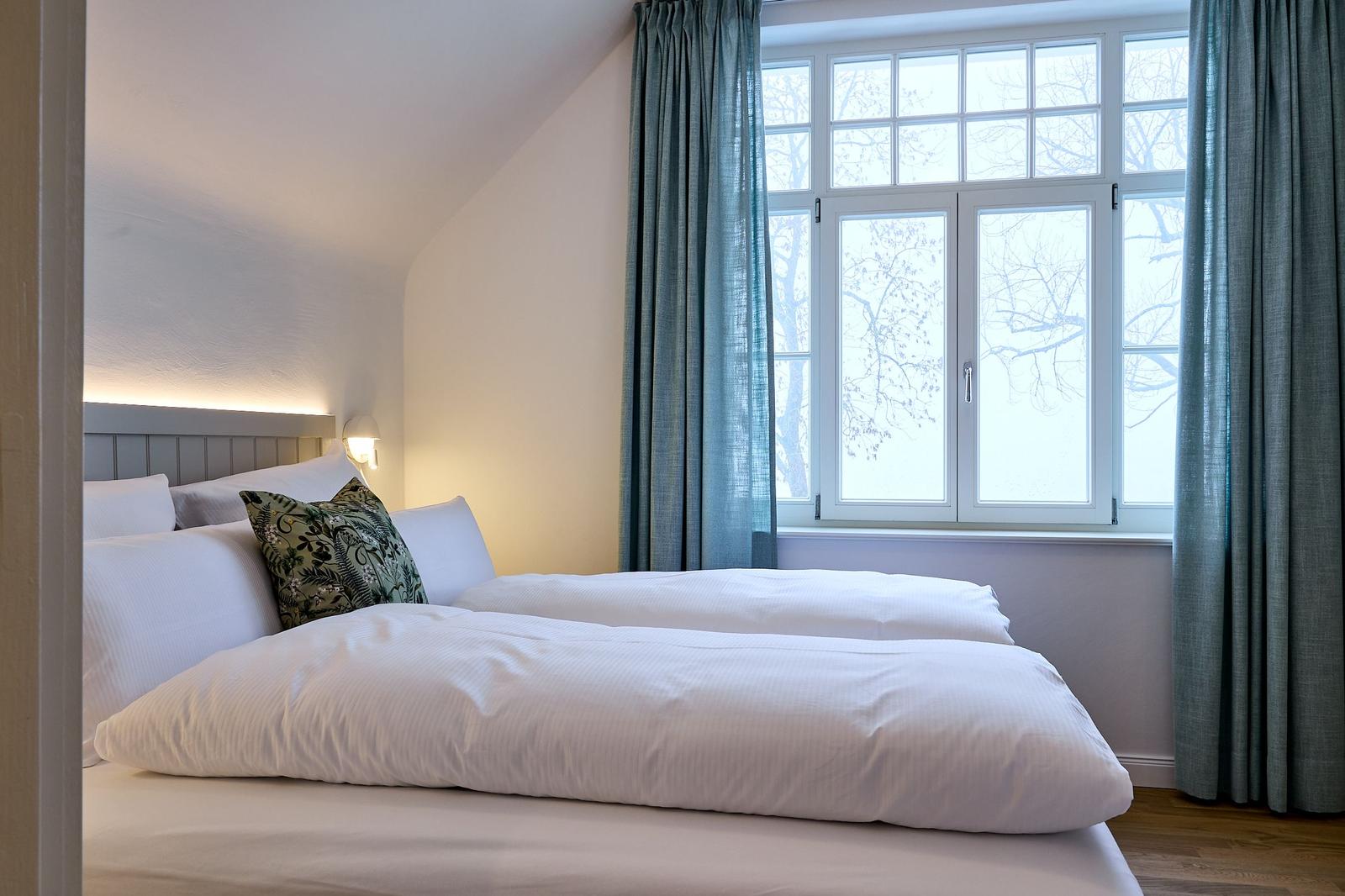 Schlafzimmer mit Bett, Fenster und Vorhängen.