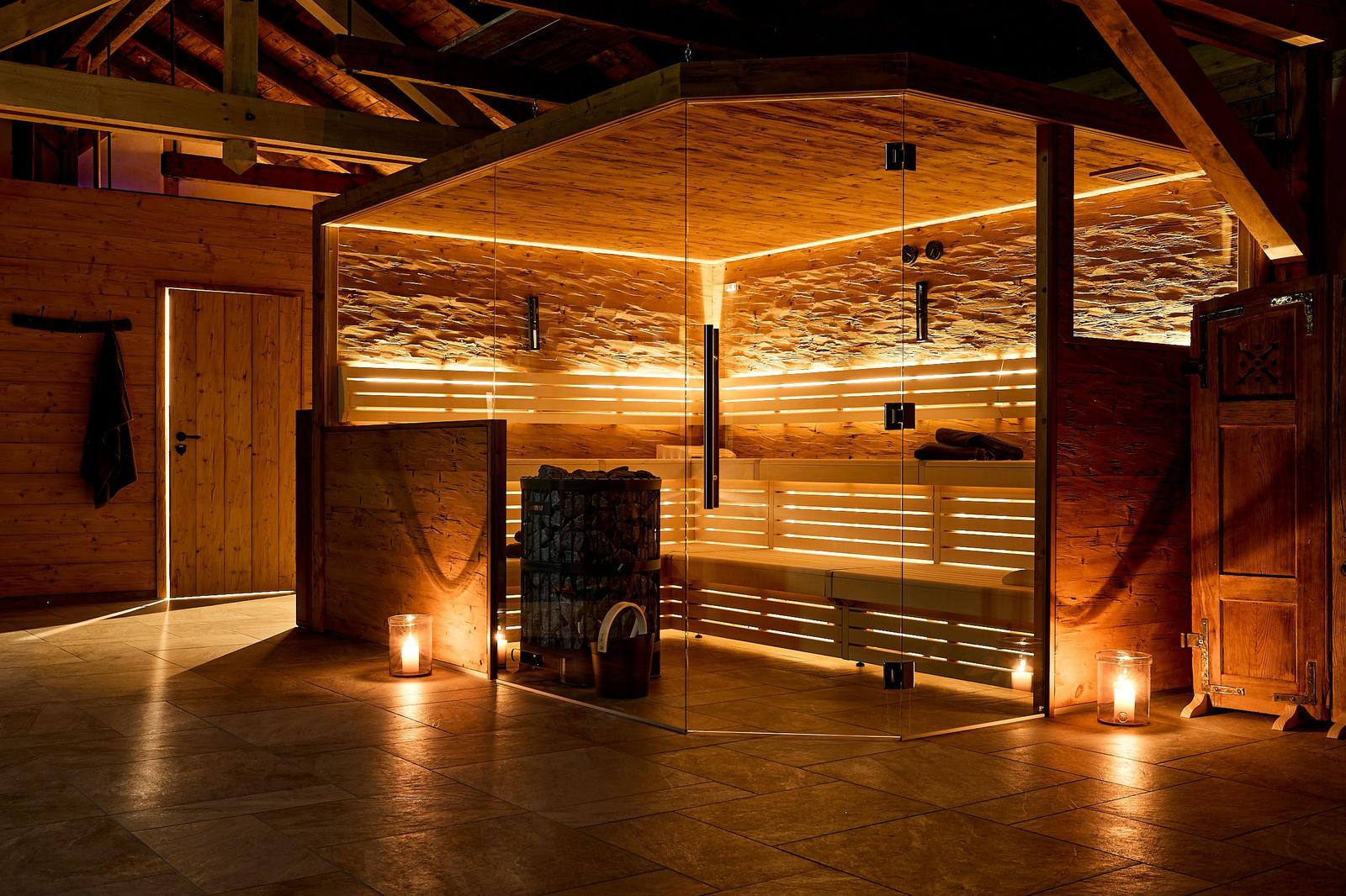 Sauna mit Holzwand und Glasfront, Beleuchtung und Bänken sichtbar.