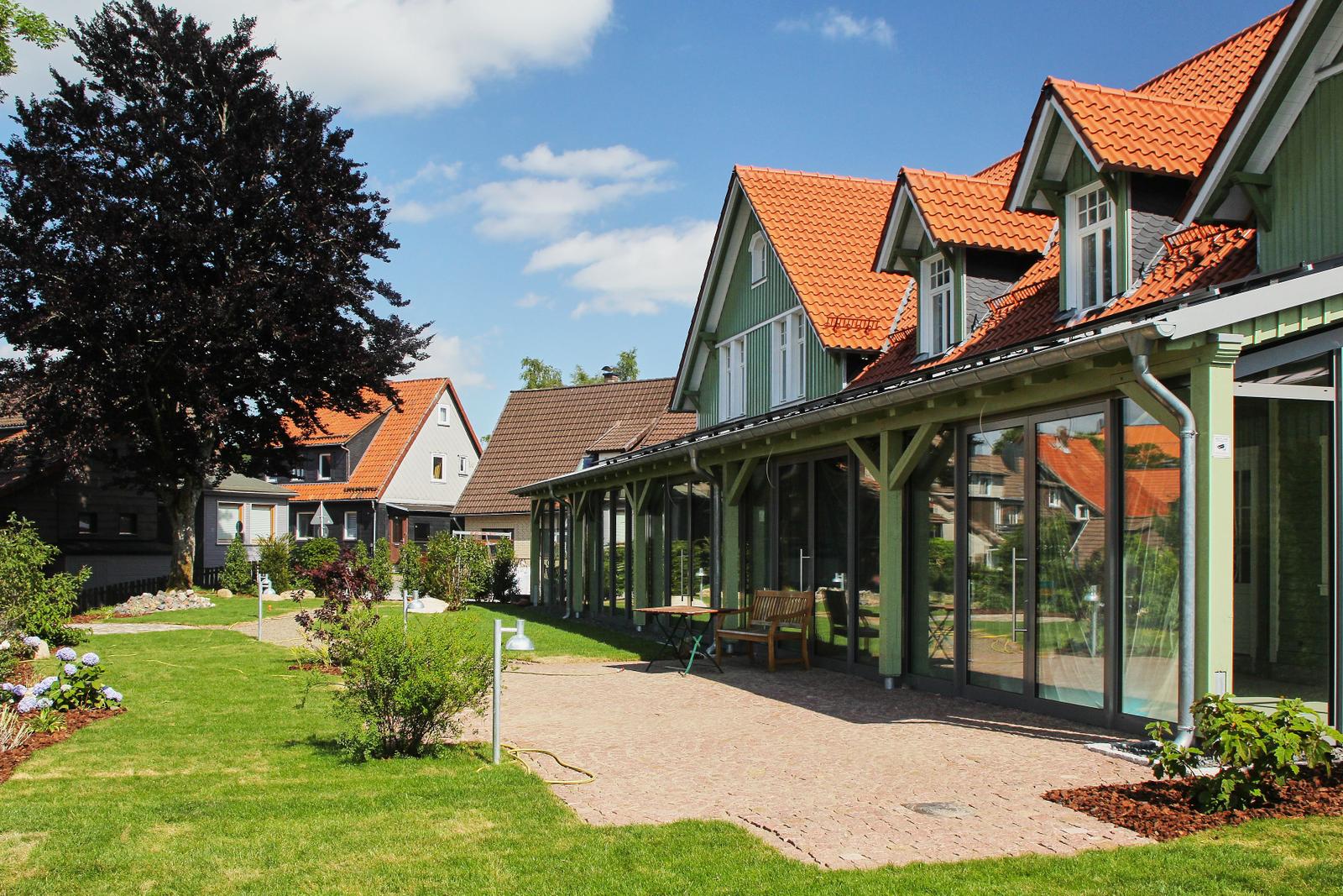 Grünes Haus mit rotem Dach und großem Glasbereich. Garten mit Rasen und Terrasse.