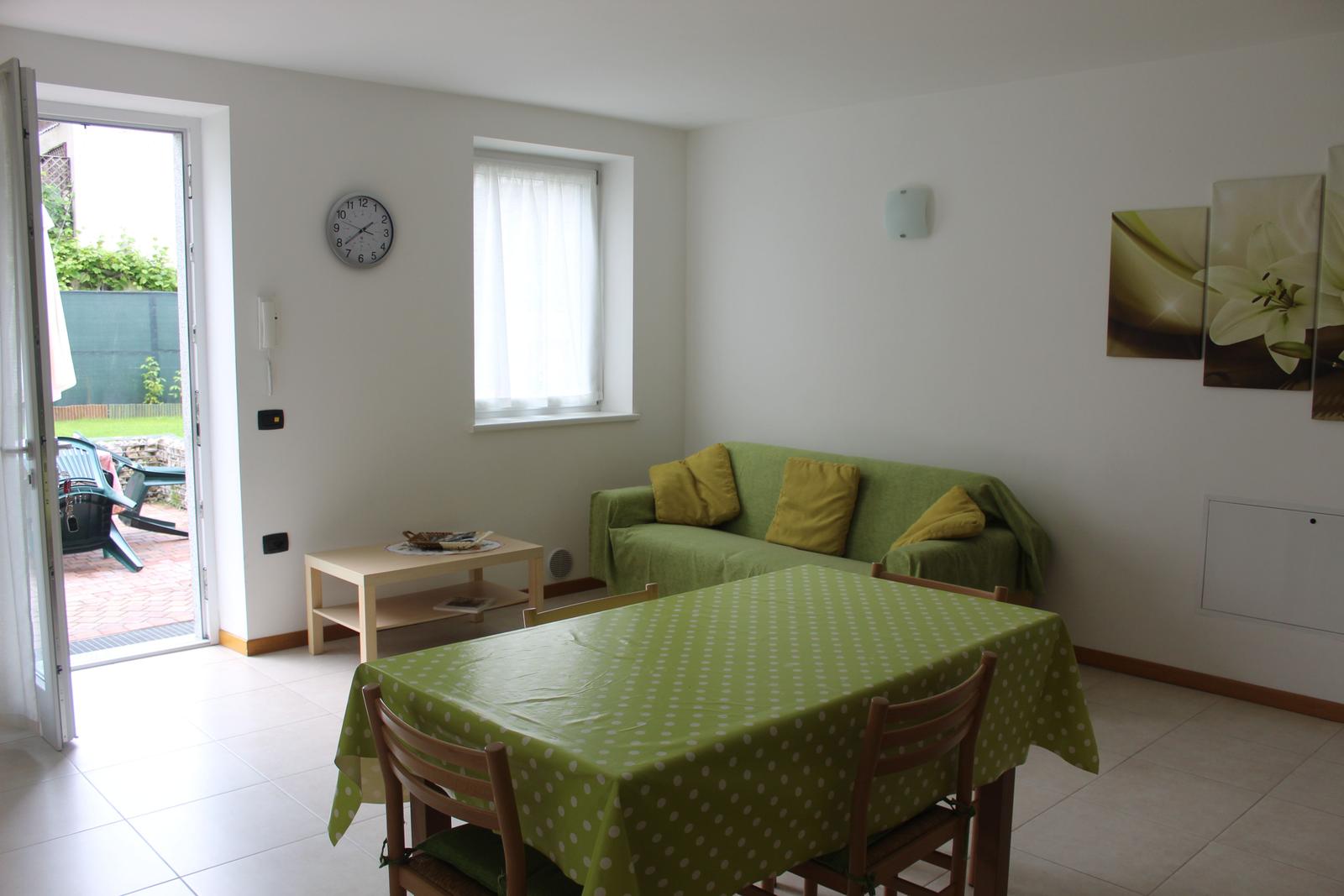 Esszimmer mit grünem Tischtuch und Sofa. Durchgang zur Terrasse.