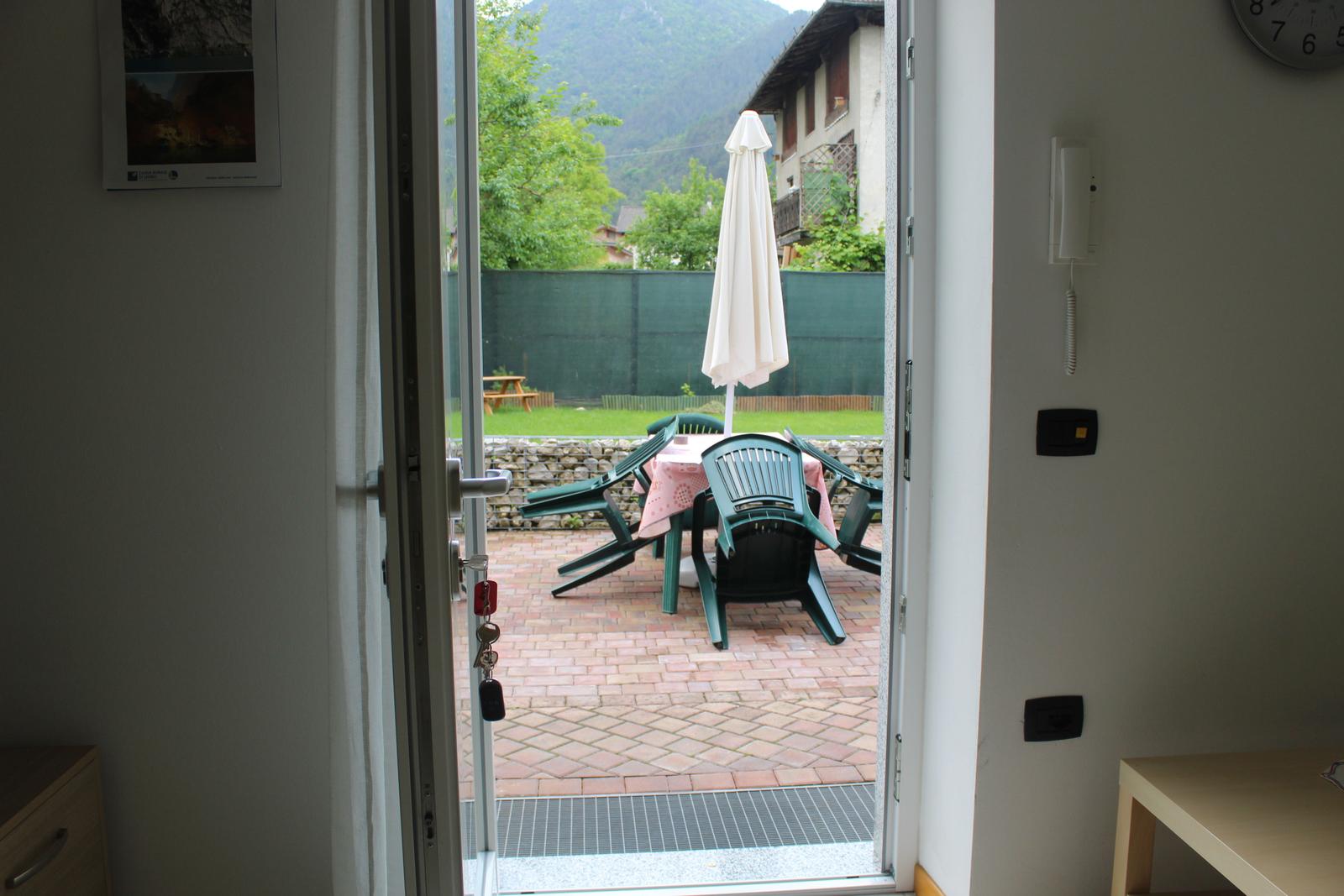 Durch die Tür ist eine Terrasse mit Tisch, Stühlen und einem geschlossenen Sonnenschirm zu sehen.