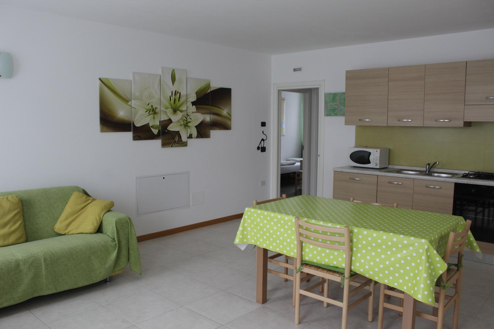 Wohn- und Essbereich mit grünem Sofa, Tisch mit Tischdecke und Küchenzeile.