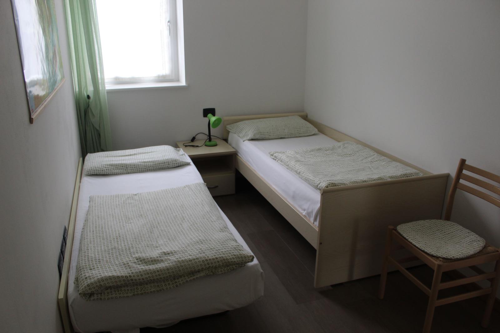 Zwei Einzelbetten, Nachttisch mit Lampe, Stuhl und Fenster.