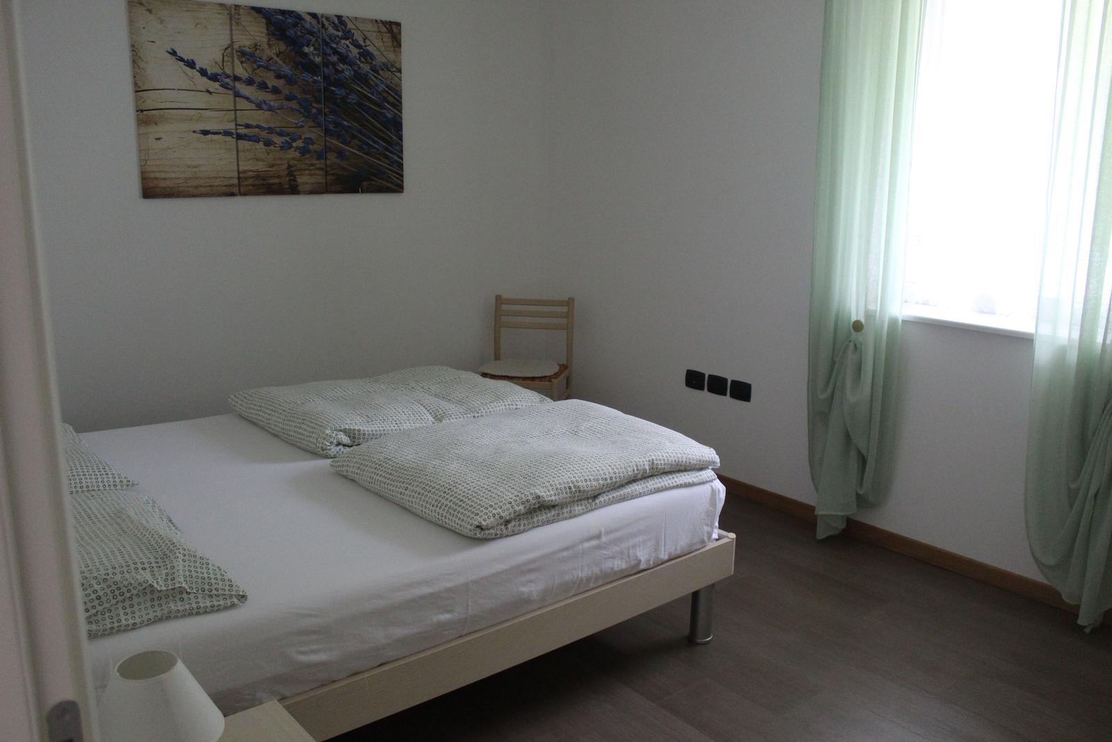 Schlafzimmer mit Bett, Stuhl und Fenster mit grünen Vorhängen.