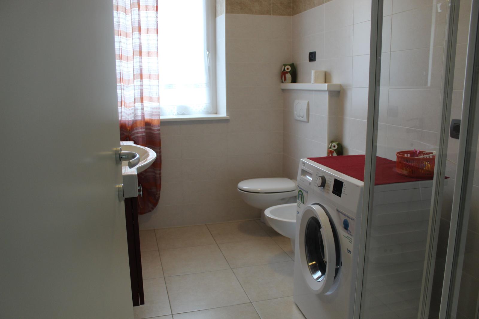 Badezimmer mit Waschmaschine, Toilette und Dusche.