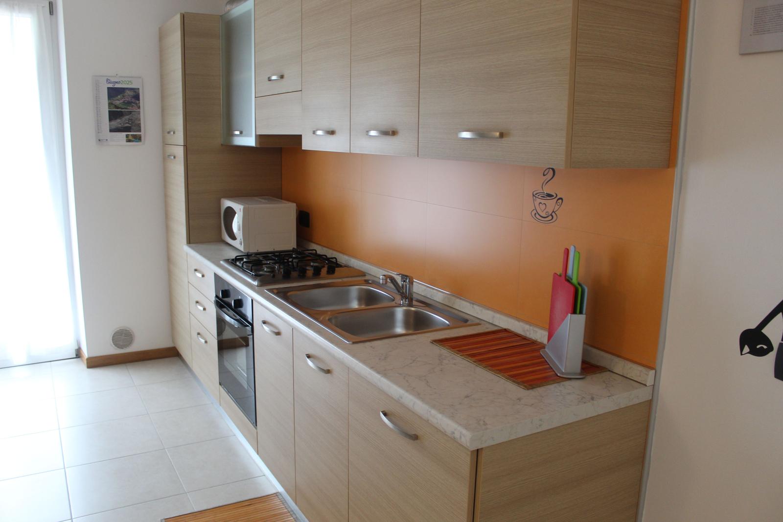 Küche mit Holzschränken, Edelstahlspüle und Mikrowelle.