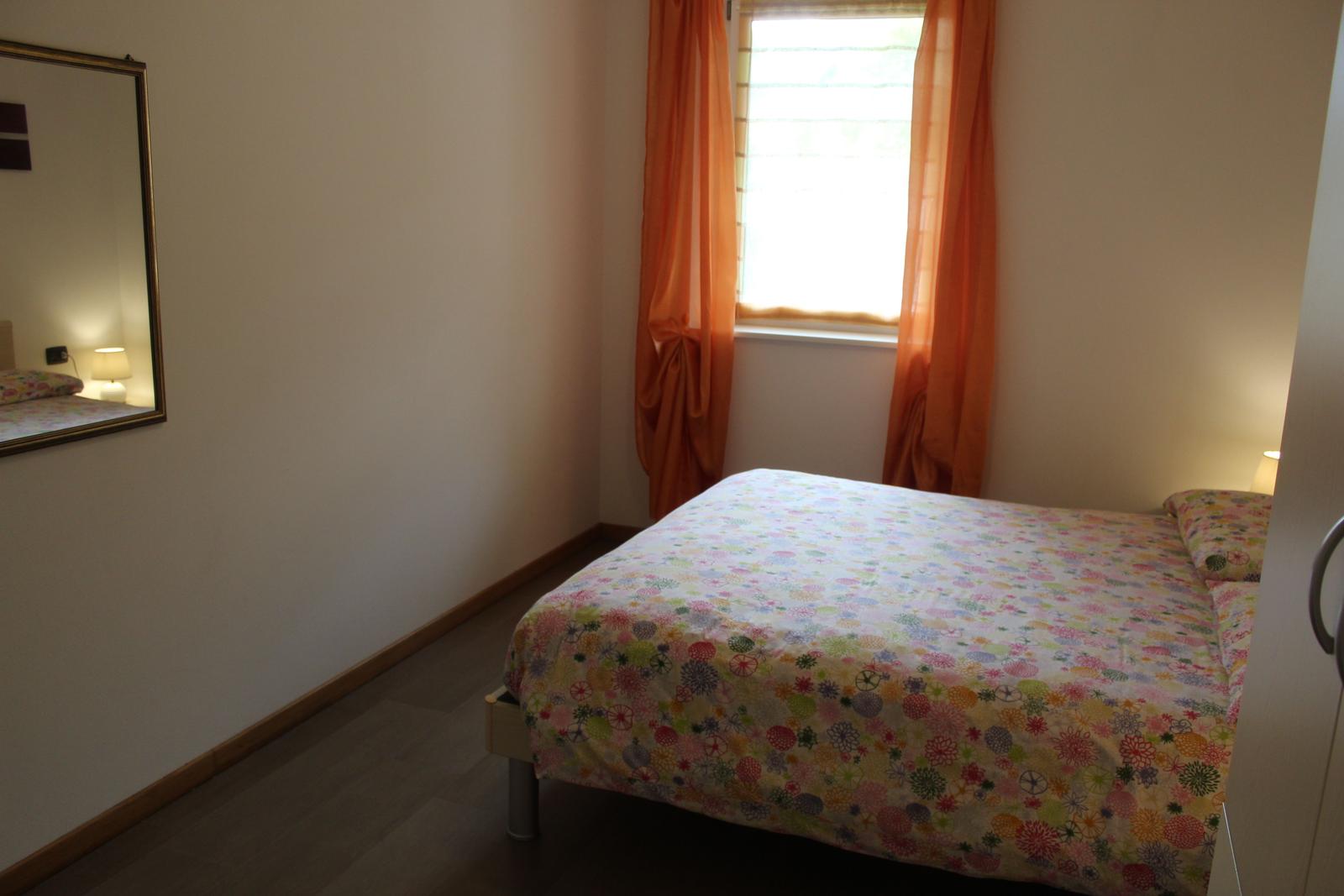 Schlafzimmer mit Bett, Fenster und Spiegel an der Wand.