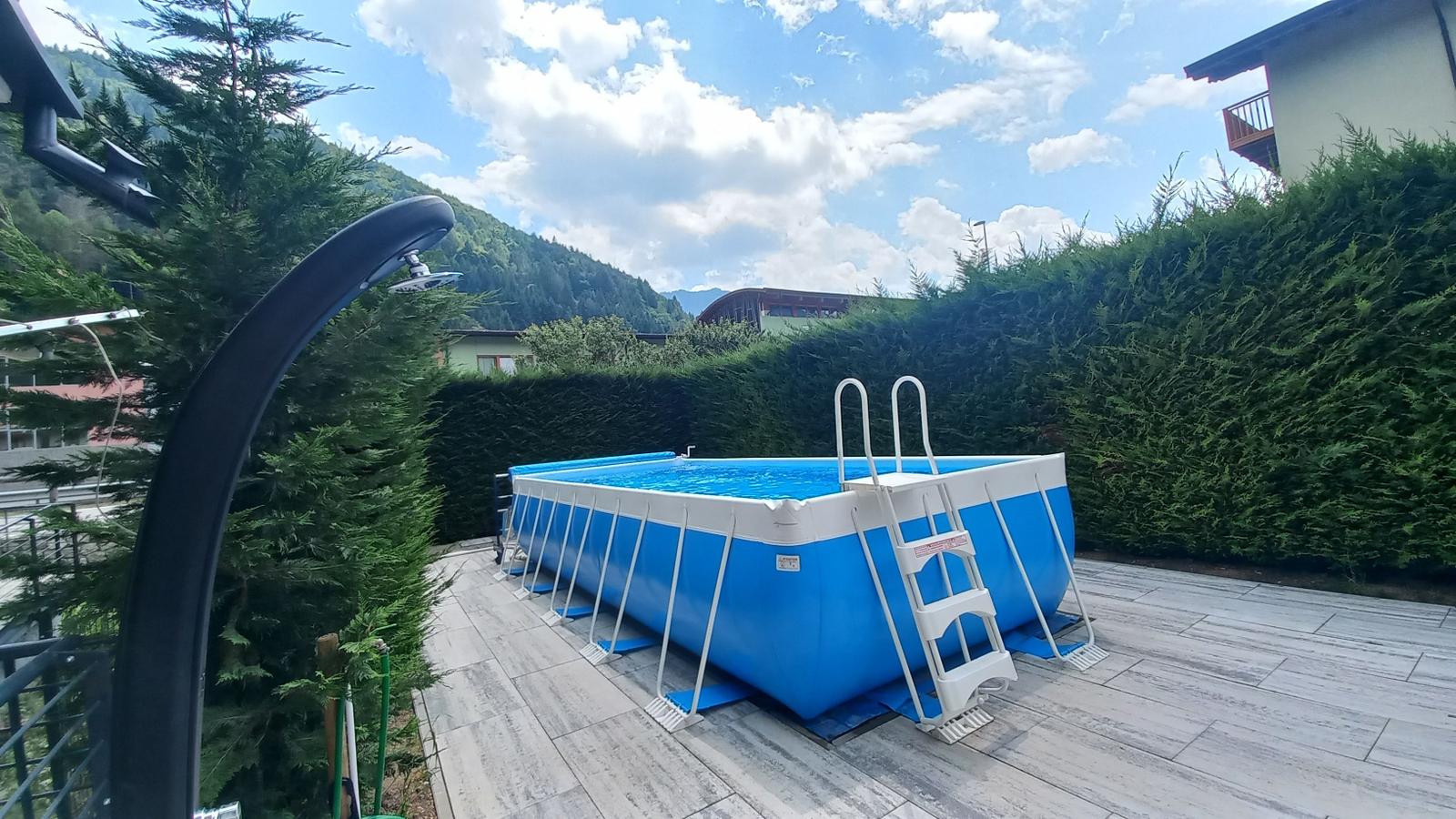 Blauer Aufstellpool auf Terrasse mit Blick auf grüne Hänge.