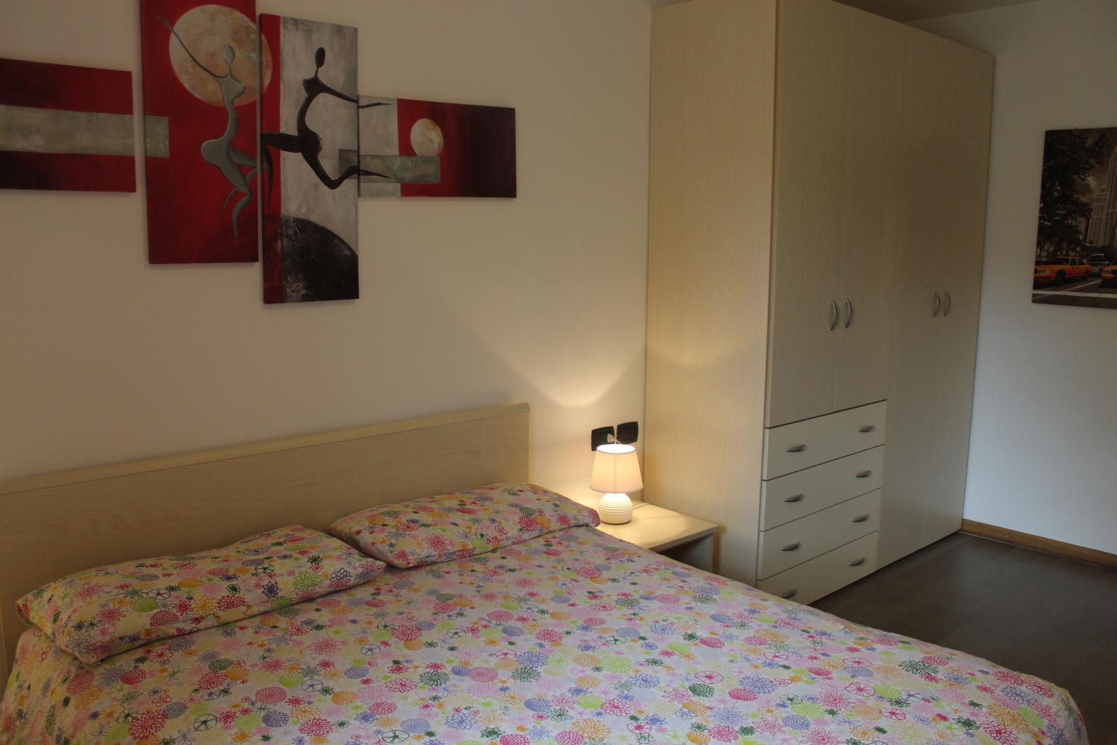 Schlafzimmer mit Bett, Nachttisch und Kleiderschrank. Wandbild mit Tanzfiguren.