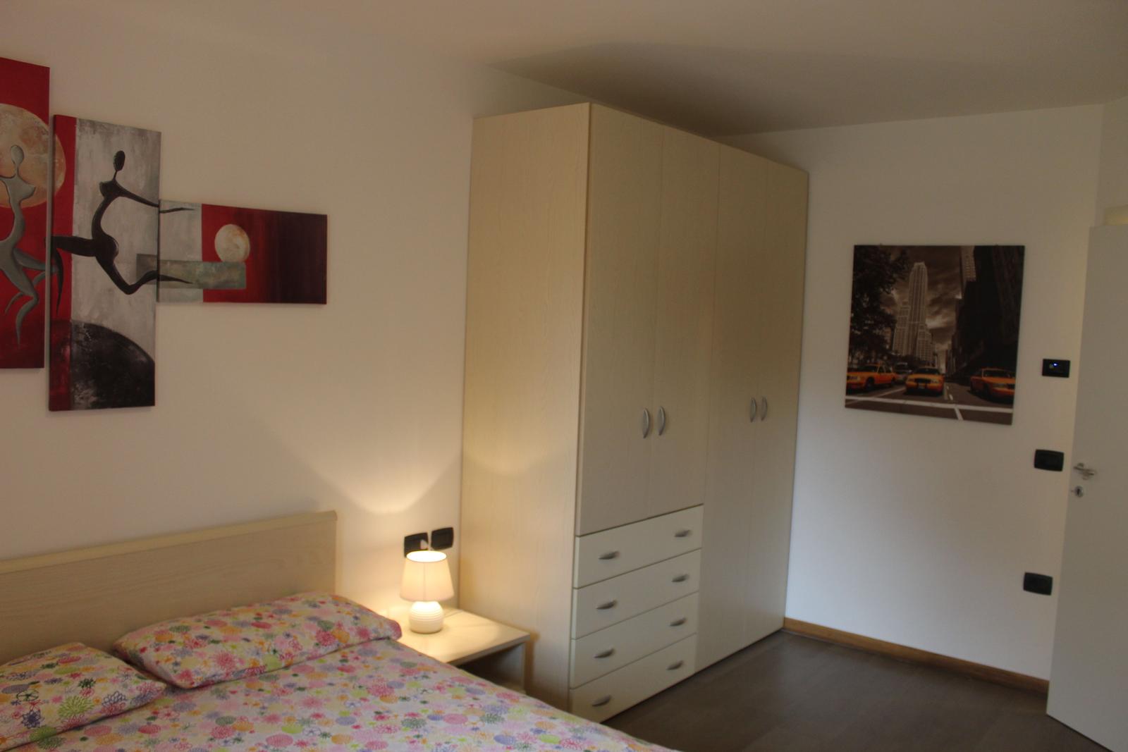 Schlafzimmer mit Bett, Kleiderschrank und Wandbildern.