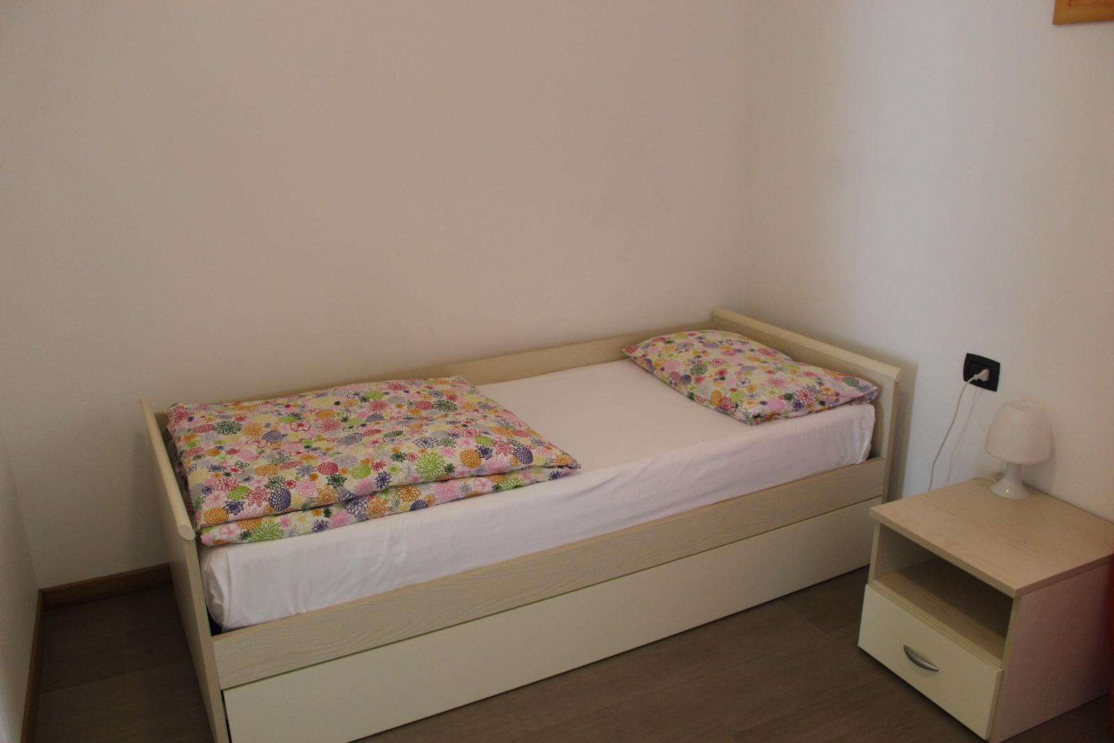 Ein Bett mit buntem Deckenbezug und Nachttisch mit Lampe.