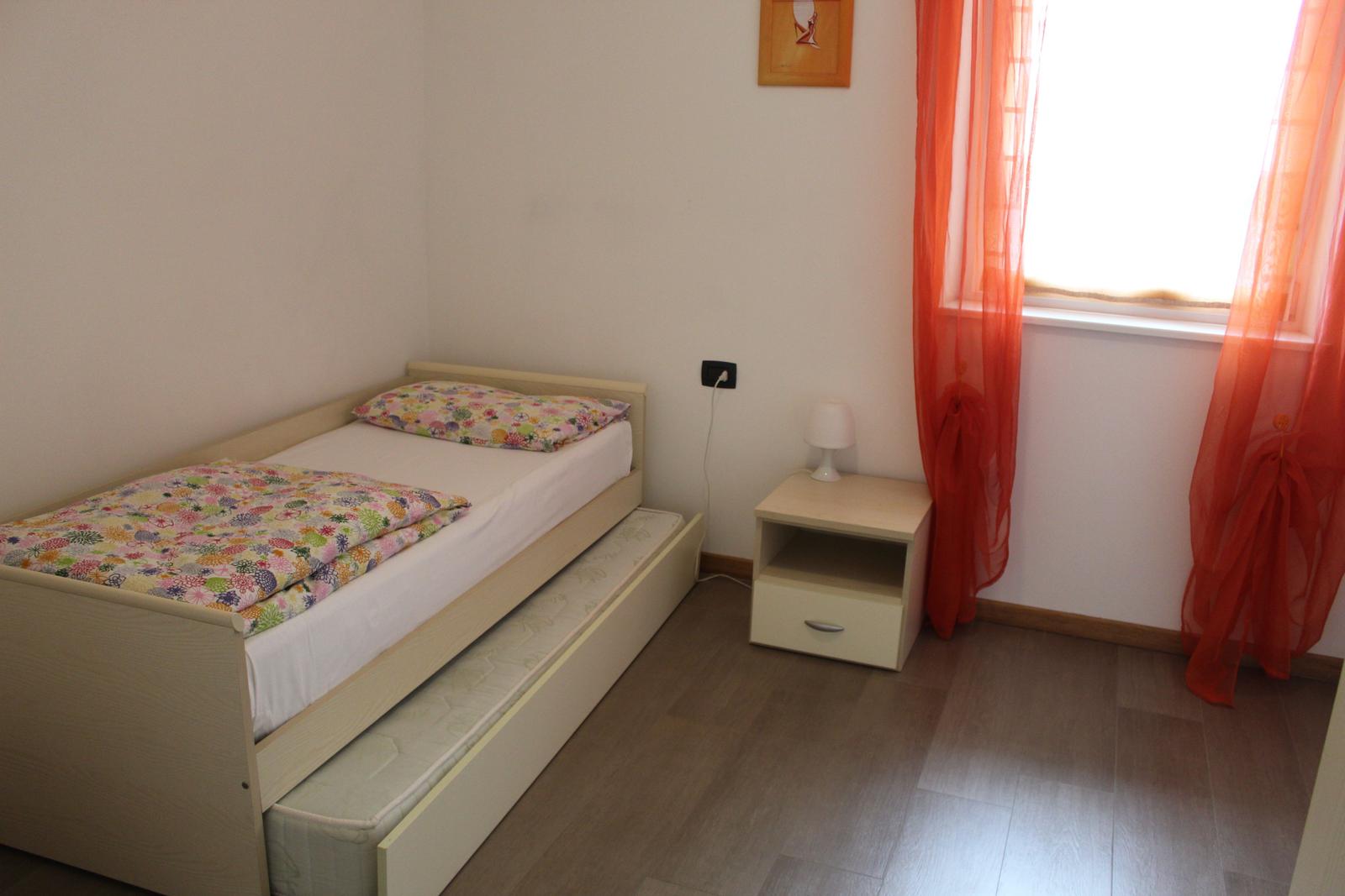 Ein Schlafzimmer mit einem Bett, einem Nachttisch und einem Fenster mit orangefarbenen Vorhängen.