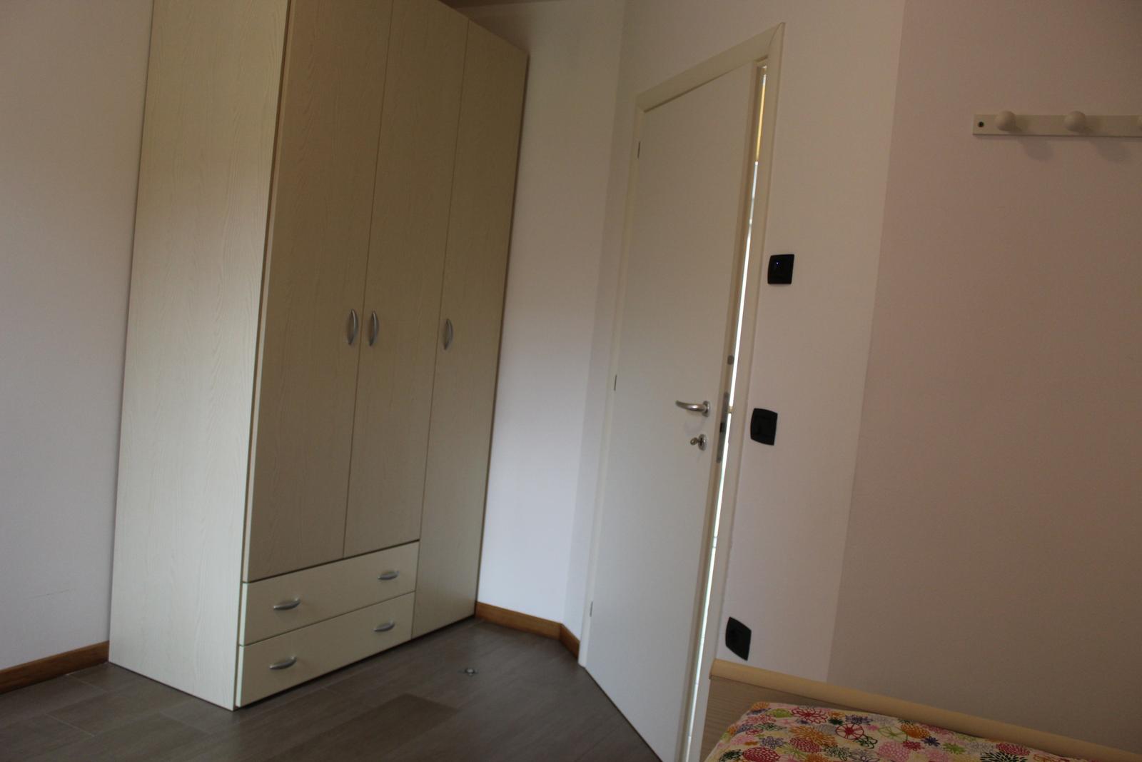 Schlafzimmer mit Kleiderschrank, Tür und Bett mit gemusterter Bettdecke.