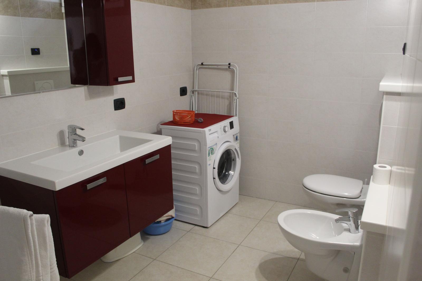Badezimmer mit Waschmaschine, Toilette und Bidet. Rot lackierte Schränke und Spiegelschrank.