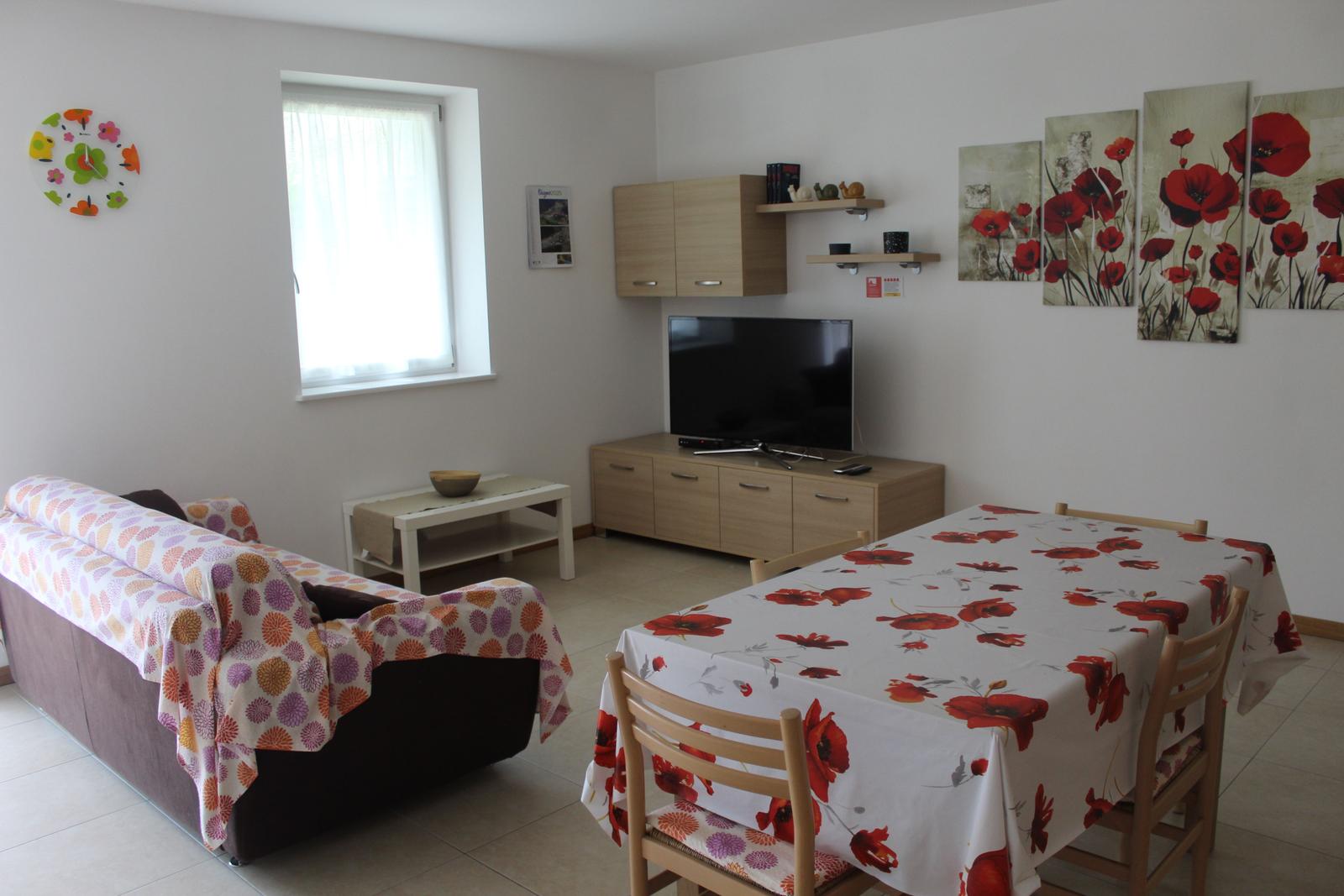 Wohn- und Essbereich mit Sofa, TV und Esstisch mit Blumentischdecke.