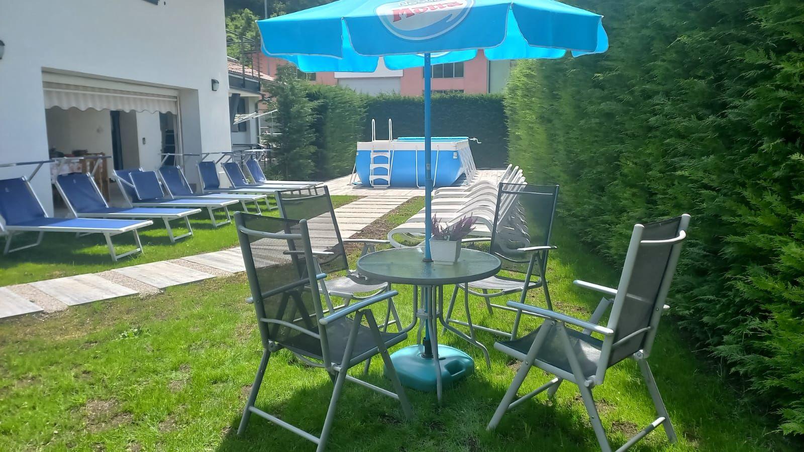 Gartenbereich mit Liegen, Pool und Tisch mit Stühlen unter einem blauen Sonnenschirm.