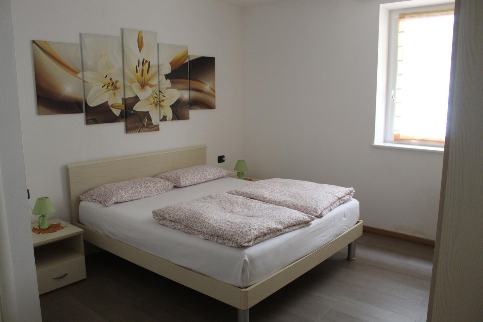 Schlafzimmer mit Bett, Nachttisch und Wandbild mit Lilien.