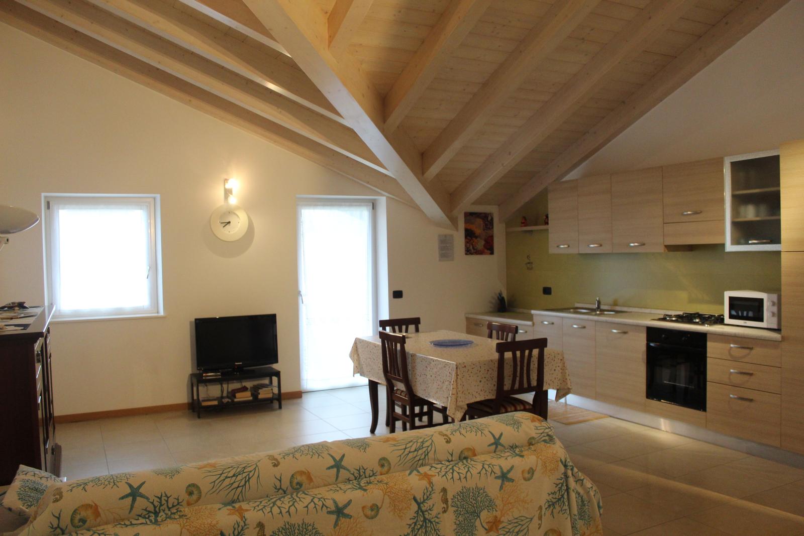 Wohnküche mit Holzbalkendecke, Esstisch, Sofa und TV.