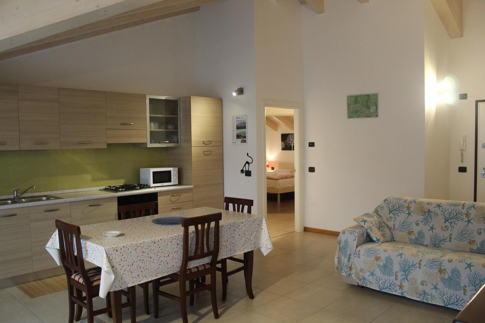 Wohnküche mit Esstisch, Sofa mit Korallenbezug und Blick in Schlafzimmer.