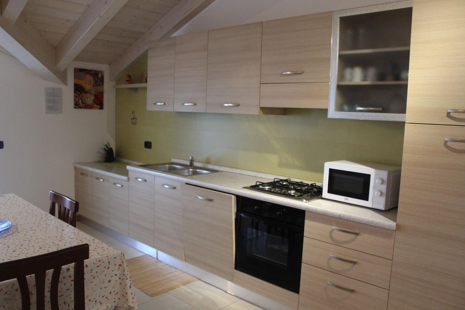 Küche mit Holzschrank, Spüle, Herd und Mikrowelle. Essbereich mit Tisch und Stühlen.