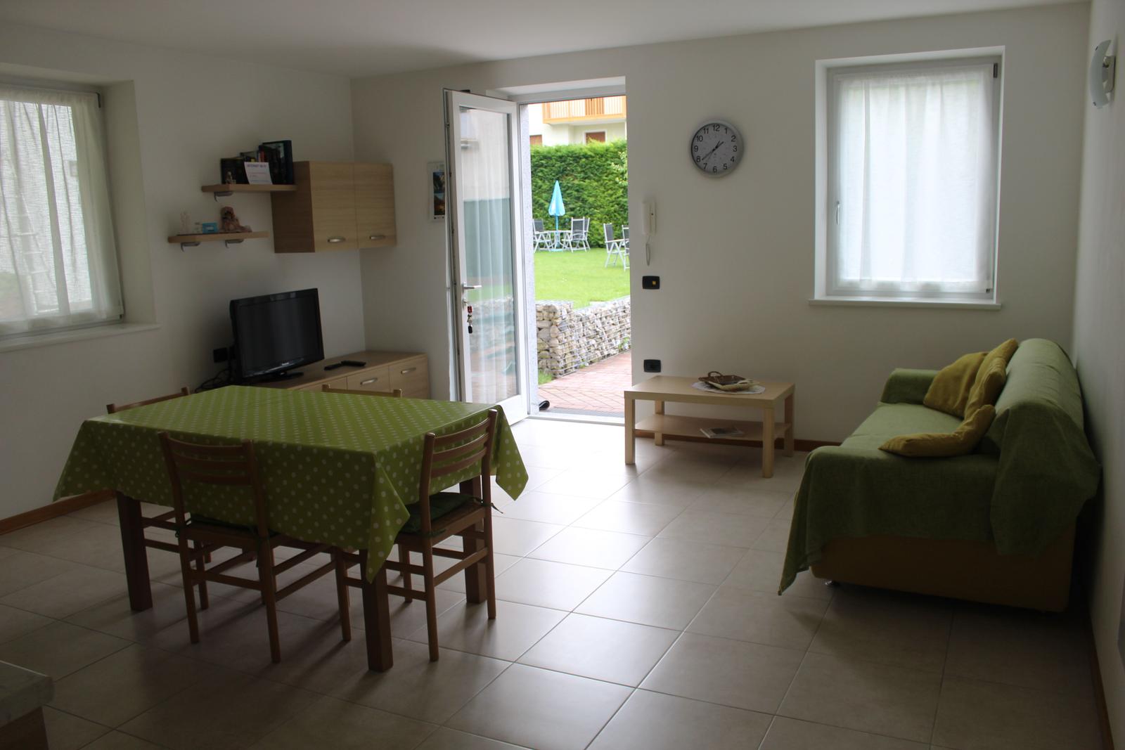 Wohn- und Essbereich mit grünem Tischdecken und Sofa, Tür zum Garten.