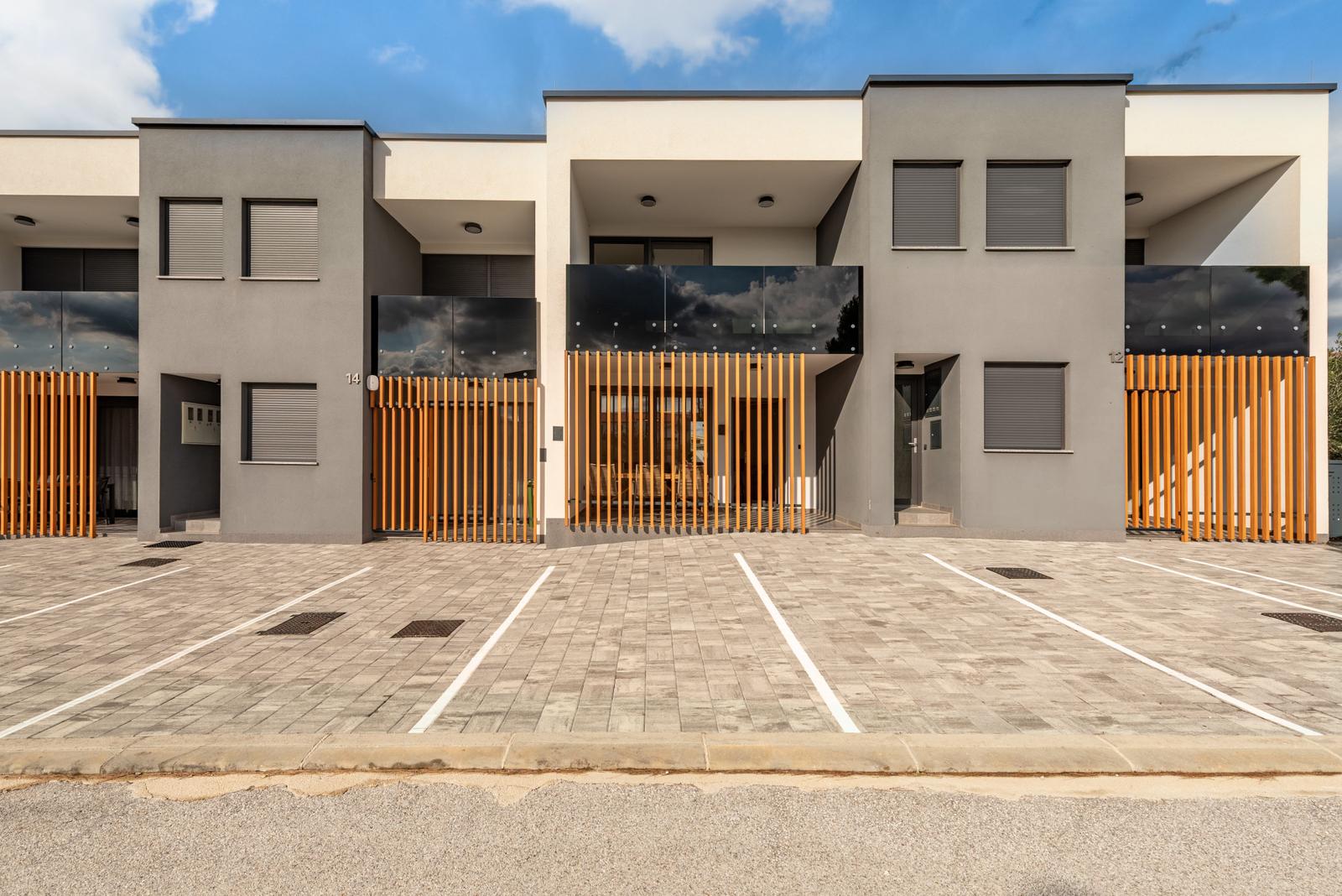 Modern villa with wooden railings and paved parking lot.