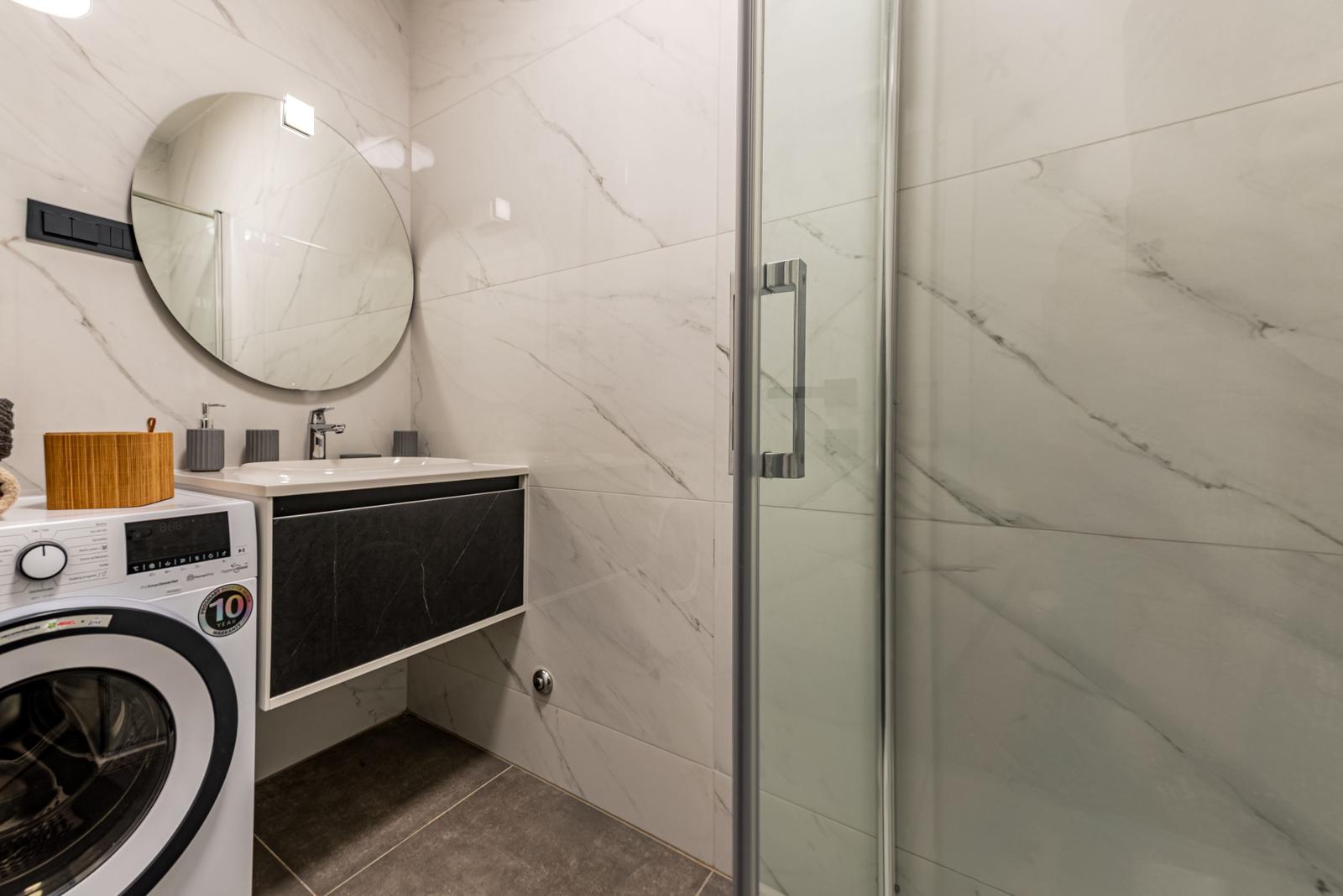 Bathroom with shower, washing machine, and sink.