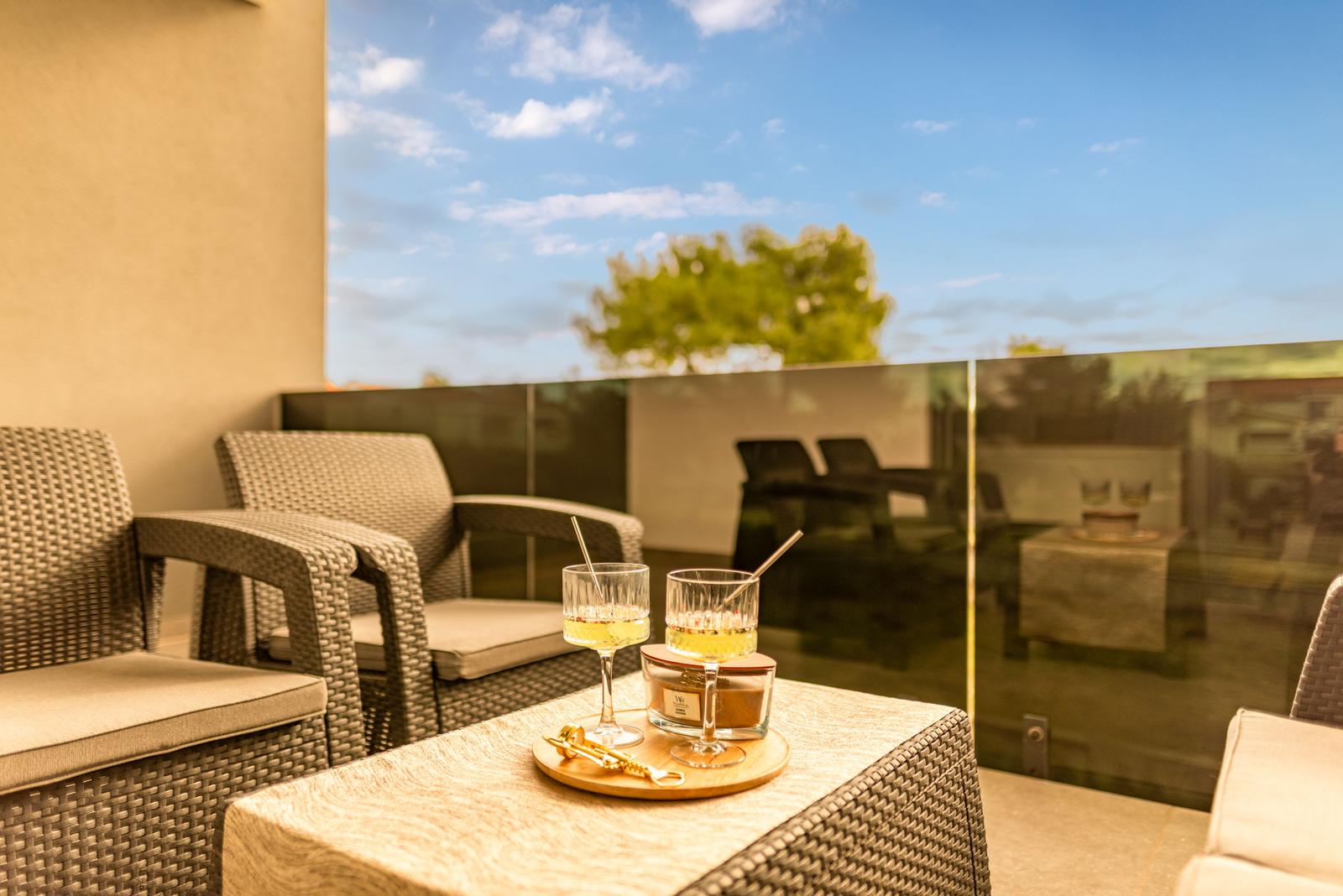 Terrace with seating and drinks. Glass railing and view of tree.