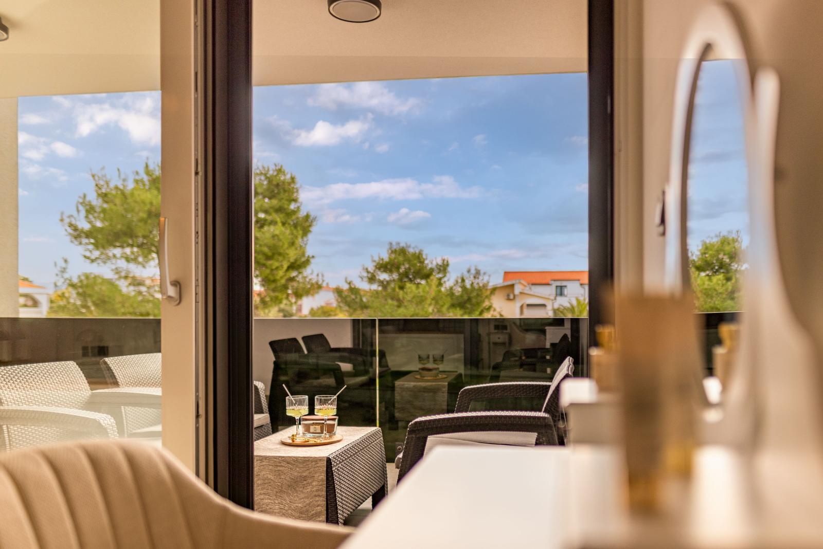 Sliding glass doors open to a terrace with seating and view of trees and buildings.