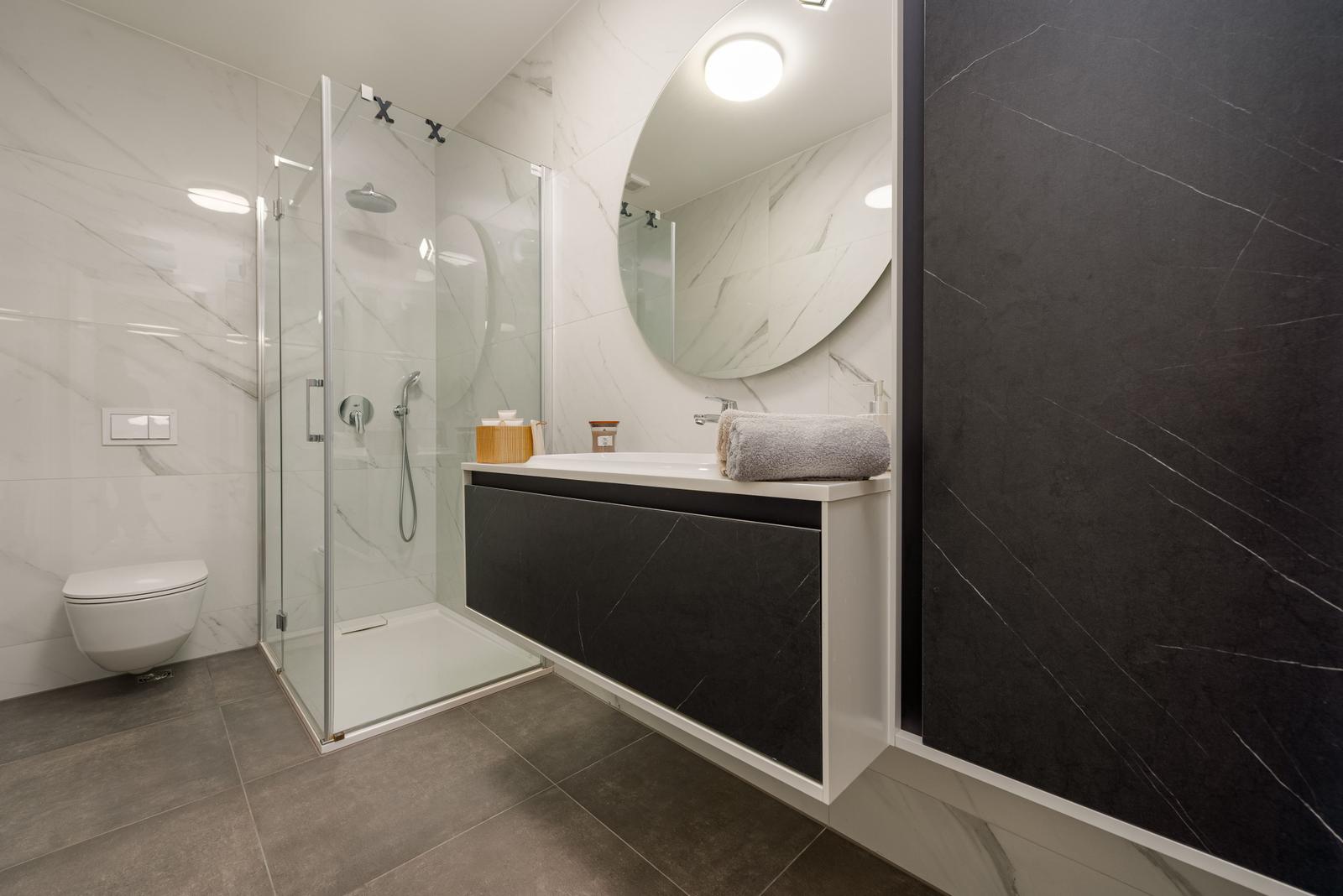 Bathroom with shower, sink and toilet. Black and white marble tiles.
