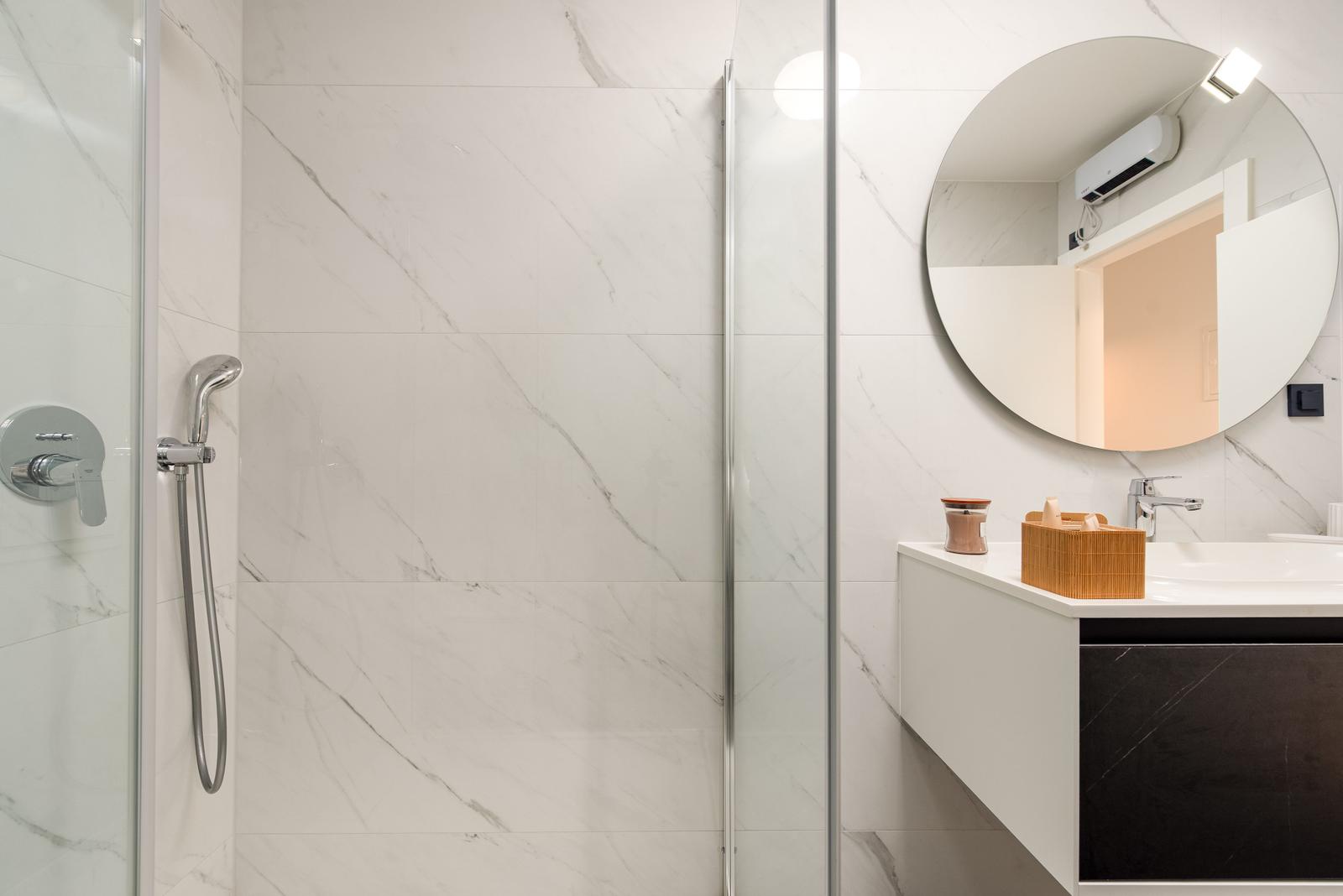 Bathroom with shower, sink, and round mirror.