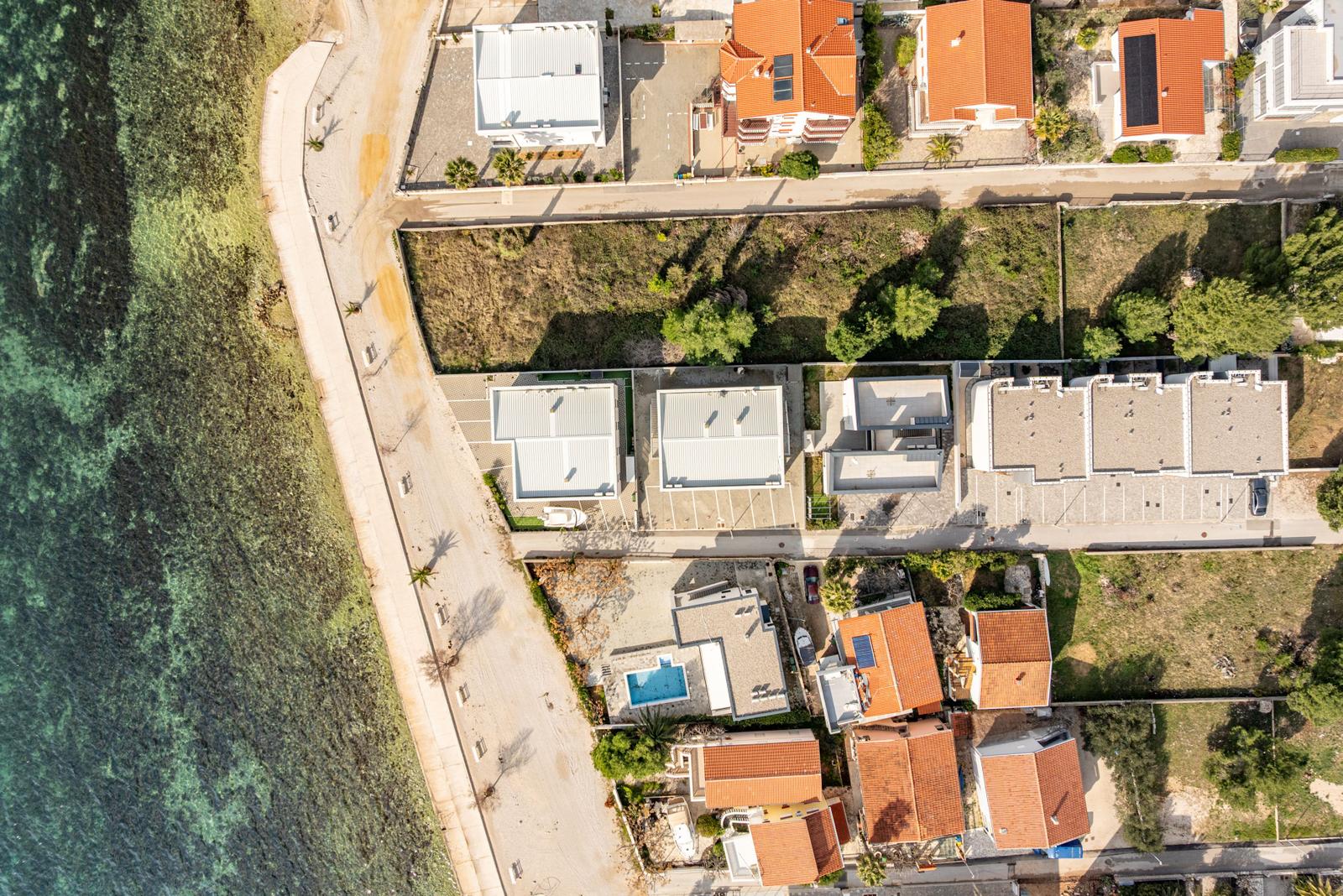 Aerial view of houses by the sea with a swimming pool and roads.