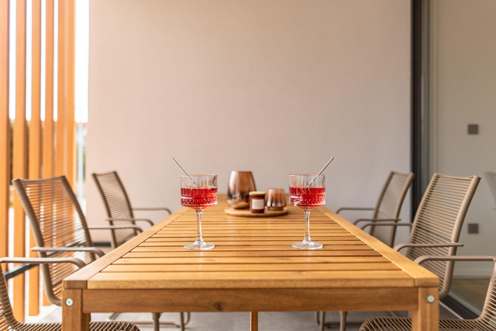 Wooden table with two glasses and chairs in the outdoor area.