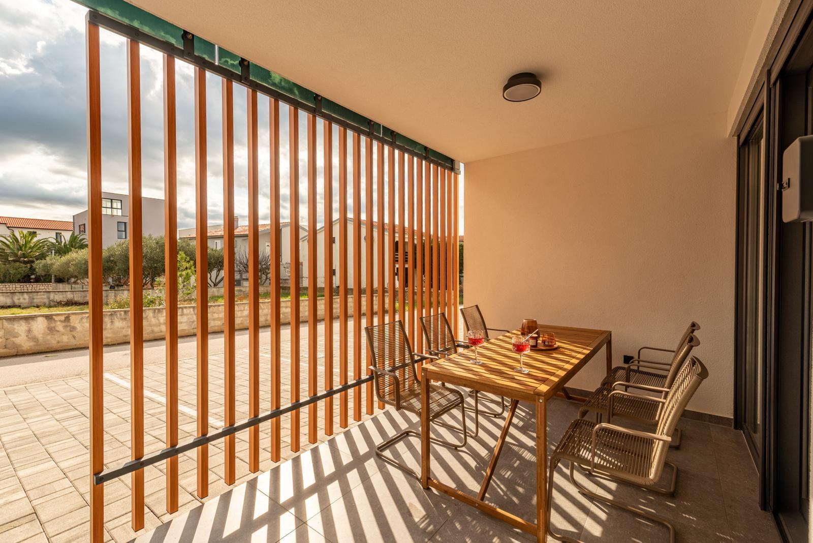 Terrace with wooden table and chairs, separated by wooden railing.