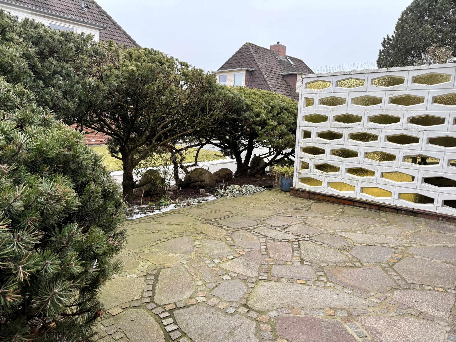 Steinplattenweg neben einer weißen Mauer mit hexagonalen Aussparungen.
