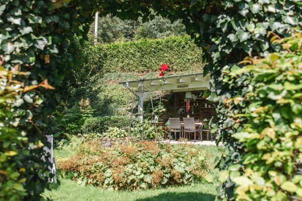 Garten mit Sitzbereich unter Pavillon, umgeben von üppiger Vegetation.