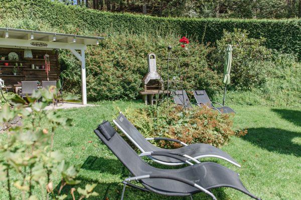 Garten mit Liegestühlen, Grill und Pavillon. Grünflächen und Hecke im Hintergrund.