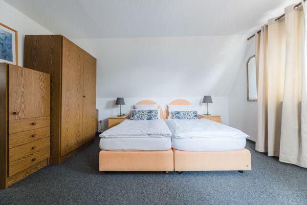 Zimmer mit Doppelbett, Holzschrank und Fenster mit Vorhängen.