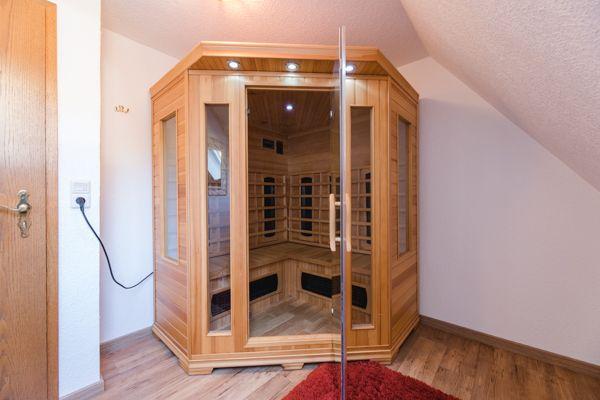 Eine Sauna mit Holzverkleidung und Glaswänden in einem Raum mit Holzboden und schräger Decke.