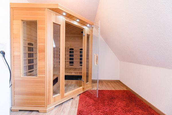 Sauna mit Holzverkleidung und Glasfront in einem Dachbodenraum mit rotem Teppich.