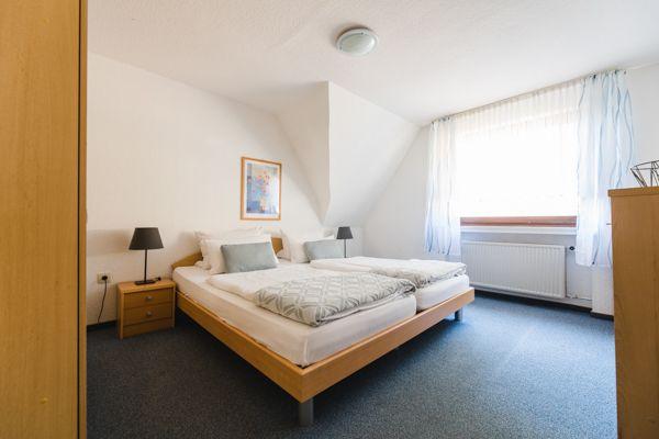 Schlafzimmer mit Doppelbett, zwei Nachttischen und Fenster mit Vorhängen.