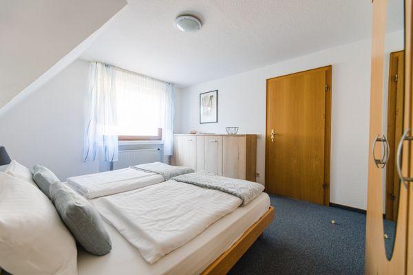 Schlafzimmer mit Dachschräge, Bett, Kleiderschrank und Fenster.