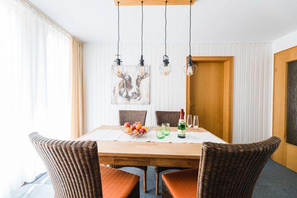 Esszimmer mit Holztisch, Stühlen und hängenden Lampen.