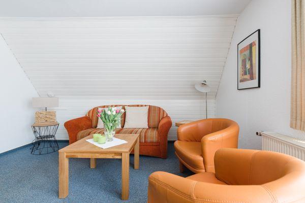 Wohnzimmer mit Sofa, zwei Sesseln und Tisch. An der Wand hängt ein Bild.