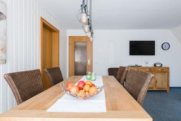 Esszimmer mit Holztisch, Stühlen und Fernseher an der Wand.